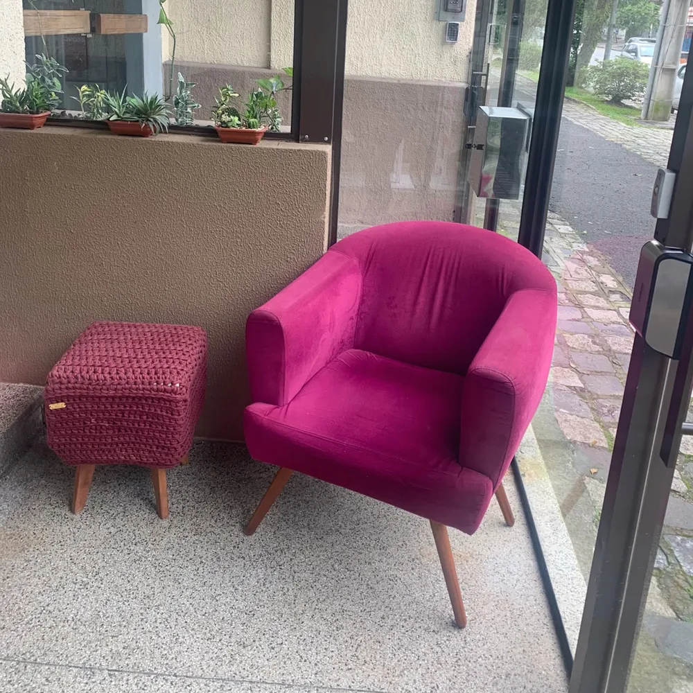 A poltrona pink e o pufe de crochê, junto à vitrine com plantas