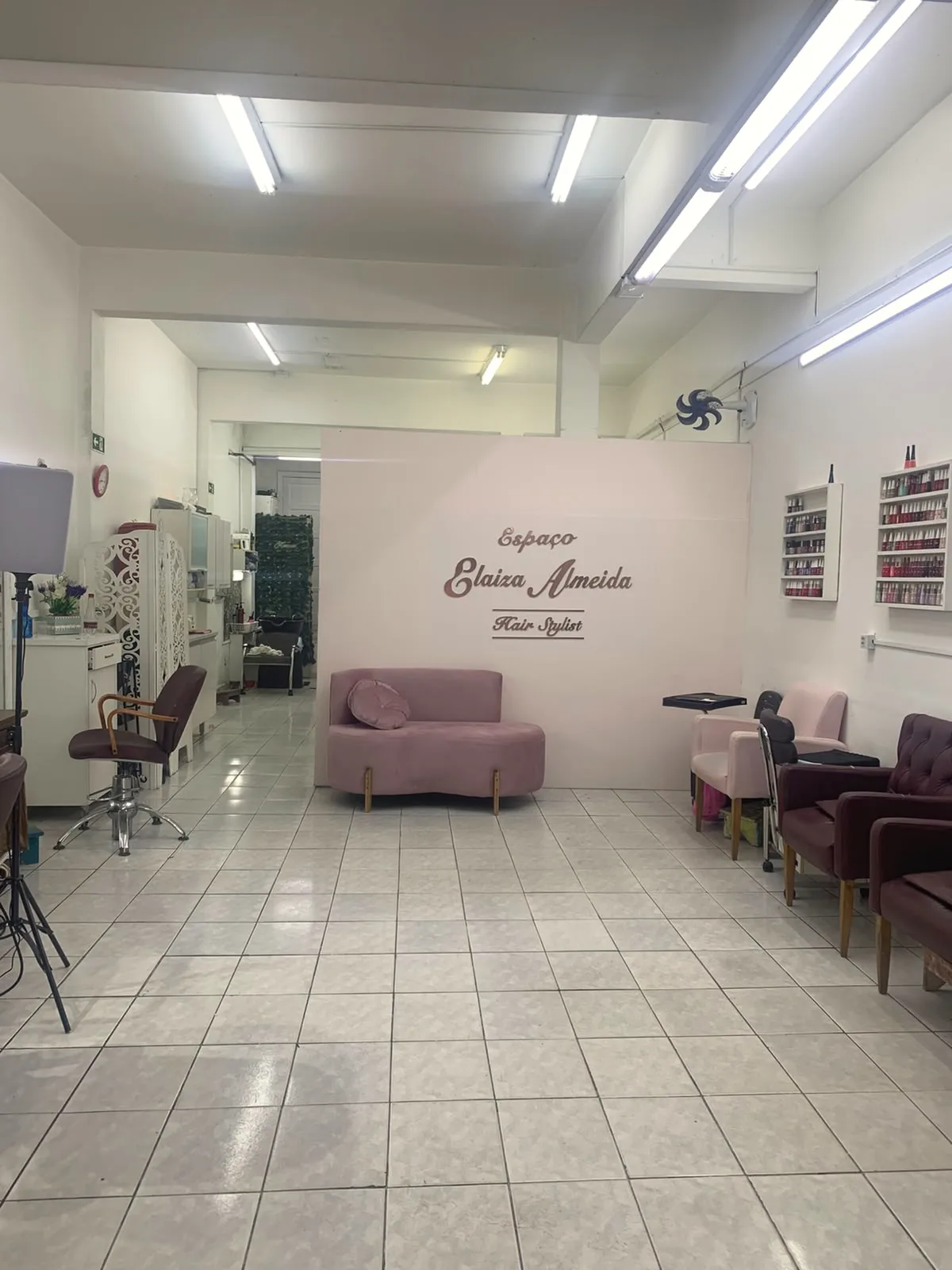 O salão por dentro: a parede rosa com o nome Espaço Elaiza Almeida, o sofá e as poltronas de espera