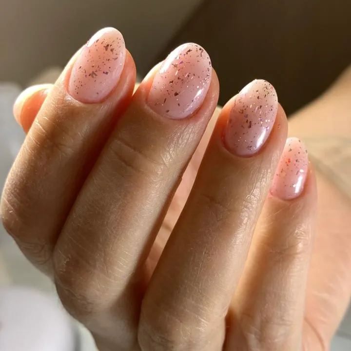 Unhas amendoadas em rosa leitoso com flocos de brilho